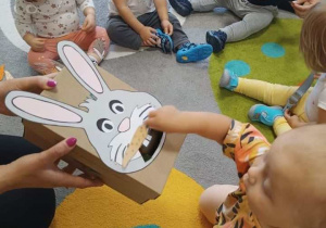Zdjęcie dzieci siedzących na dywanie podczas zabawy z pudełkowym królikiem.