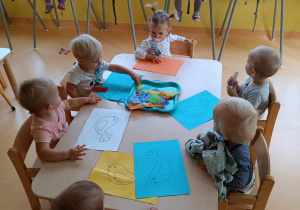 Zdjęcie dzieci z grupy Motylki siedzących przy stoliczku i przygotowujących się do zajęć plastycznych pt. ,,PIÓRKOWE PTASZKI''.