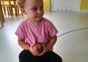 Kornelia siedząca na podłodze z jabłkiem.