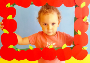 Kornelia pozuje do zdjęcia w ramce z papierowych, czerwonych jabłek.