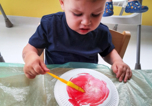 Zdjęcie Filipka malującego czerwoną farbą papierowy talerzyk.