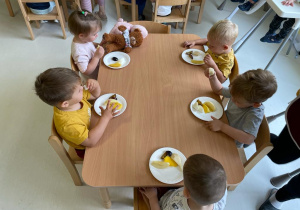 Dzieci z grupy Żabki siedzące przy stole próbują wczesniej poznanych owoców.