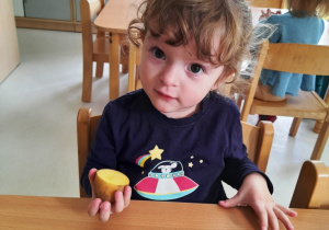 Rozalia siedzi przy stole trzymając w ączce połówkę ziemniaczka.
