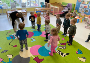 Dzieci wraz z opiekunką bawia się na dywanie.
