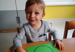 Uśmiechnięty Fabianek pozuje do zdjęcia z szablonem pomidorka wydrukowanym na zielonej kartce.