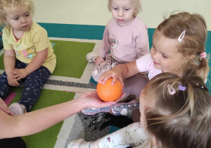 Laura, Aleksandra, Iga oraz Lilianna oglądają dużą pomarańczę, którą trzyma w dłoni opiekunka.