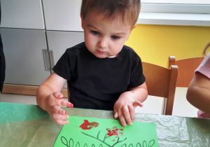 Olaf podczas stemplowania palcem i czerwoną farbą na zielonej kartce.