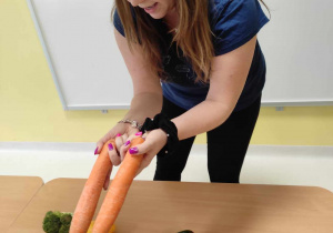 Opiekunka pokazuje dzieciom dwie duże marchewki.