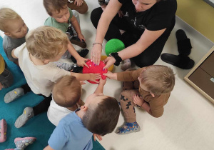Dzieci dotykają czerwony dysk sensoryczny trzymany przez opiekunkę.