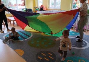 Zdjęcie dzieci i opiekunek na dywanie podczas zabawy z chustą animacyjną.