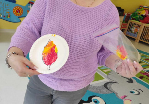 Opiekunka pokazuje dzieciom jak ma wyglądać listek z rozprowadzoną farbą.