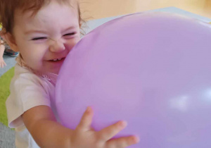 Uśmiechnięta Maja trzyma w dłoniach fioletowego nadmuchanego balonika.