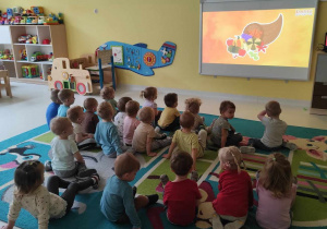 Zdjęcie dzieci siedzących na dywanie podczas oglądania edukacyjnej bajki pt.,, Kazio i Dzień Dyni''.