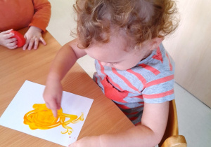 Dziewczynka miesza paluszkiem farby, aby powstał kolor pomarańczowy.