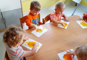 Maluchy siedzące przy stoliku podczas zajęć z farbami.