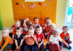 Pamiątkowe zdjęcie dzieci z grupy Biedroneczki przed pomarańczową ścianką.