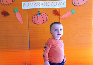 Mały chłopiec pozujący na tle ścianki z okazji Dnia Pomarańczowego.