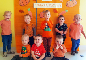 Pamiątkowe zdjęcie chłopców z grupy Biedroneczki ubranych na pomarańczowo pozujących na tle ścianki.