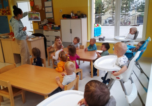 Opiekunka pokazuje dzieciom siedzącym przy stole obrazek z wiewiórką.