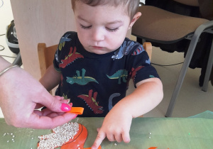 Chłopczyk z pomocą opiekunki przykleja na ogon wiewiórki kawałki pomarańczowego papieru.