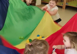 Dzieci bawią się kolorowymi kulkami w chuście.
