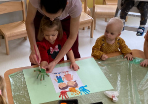 Opiekunka maluje zieloną farbą dłoń dziewczynki.