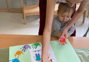 Opiekunka maluje czerwoną farbą dłoń małego chłopca.