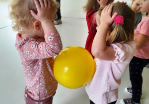 Dziewczynki z balonikiem umieszczonym między nimi tańczą do piosenki.