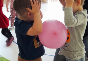 Dwóch chłopców tańczących z różowym balonem umieszczonym pomiędzy nimi.