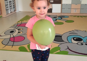 Dziewczynka trzymająca w dłoniach zielony balonik.