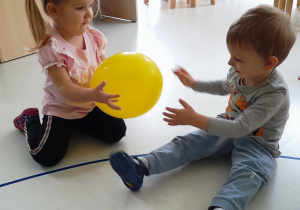 Mała dziewczynka podaje żółty balon koledze.