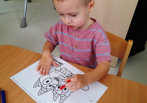 Chłopiec koloruje na czerwono postać z bajki.