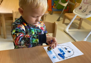 Chłopiec wykonuje gabeczką umoczoną w niebieskiej farbie swojego potworka.