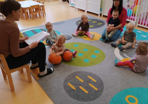 Zdjęcie dzieci i opiekunek z grupy Motylki siedzących na dywanie podczas czytania bajek na dywanie.