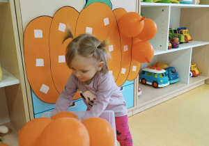 Marcelina wyciąga z plastikowego pudełka nadmuchany pomarańczowy balon.
