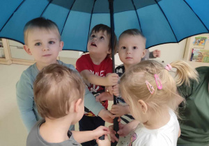 Zdjęcie dzieci trzymających wspólnie niebieską parasolkę.