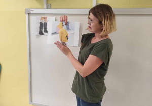 Opiekunka prowadząca zajęcia pokazuje dzieciom obrazek przedstawiający zdjęcie żółtego płaszcza przeciwdeszczowego.