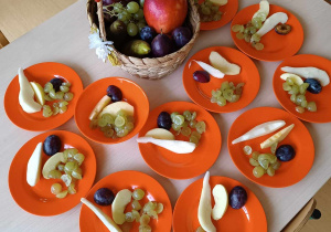 Zdjęcie pomarańczowych talerzyków z naszykowanymi dla dzieci owocowami.