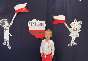 Chłopiec, który stoi przed ścianką zrobioną z okazji Dnia Niepodległości.