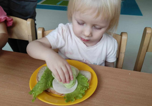 Aleksandra kładzie na swoją kanapeczkę plasterki zielonego ogórka.