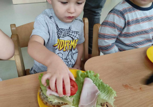 Leon kładzie na swoją kanapeczkę plasterek pomidora.