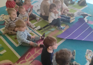 Zdjęcie dzieci siedzących na dywanie, słuchających opiekunkę opowiadającą o Piramidzie Zdrowego Żywienia.