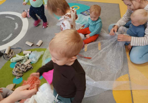 Zdjęcie dzieci i opiekunki z grupy Motylki siedzących na dywanie podczas zajęć pt. ,,BAWIMY SIĘ W ODKRYWCÓW''.