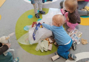 Zdjęcie dzieci poszukujących ukrytych zabawek pod rozłożonymi na dywanie materiałami.
