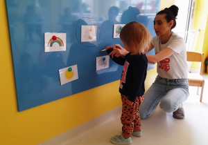 Opiekunka pomaga dziewczynce obrysować ilustrację z symbolem wiatru.