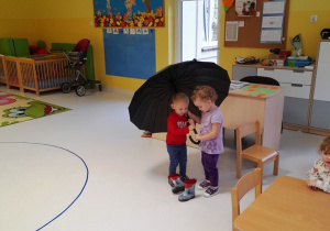 Dwoje dzieci chowa się pod parasolem.
