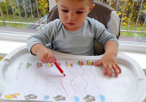 Chłopczyk rysuje czerwoną kredką.