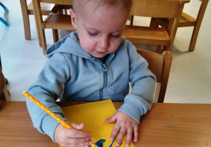 Chłopczyk rozmazuje słomką farbę na kartce.