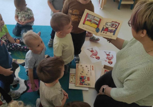 Zdjęcie dzieci słuchających na dywanie czytającej bajkę opiekunki pt. ,,KICIA KOCIA poznaje Strażaka''.