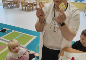 Opiekunka pokazuje dzieciom zabawkowe drewniane tabletki.